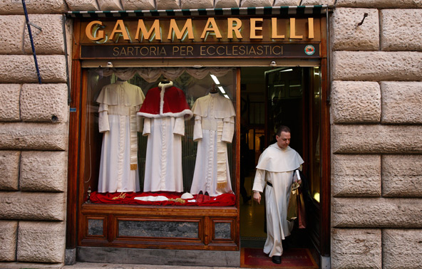 Three sizes of cassocks for the future pope are displayed in the window of the Gammarelli clerical tailor shop in Rome March 4. At the request of the Vatican the famous shop has prepared three sizes of clerical wear to be used by the new pope immediately after his election. Pictured leaving the store is Dominican Father Thomas Petri, assistant professor of theology at Providence College in Rhode Island. (CNS photo/Paul Haring)