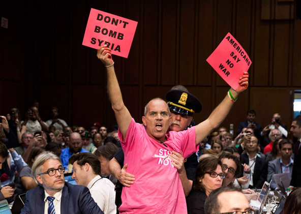 A protester waves signs as Obama administration officials arrive to present the case for U.S. military action against Syria to a Senate Foreign Relations Committee hearing on Capitol Hill in Washington Sept. 3. (CNS photo/Joshua Roberts, Reuters)