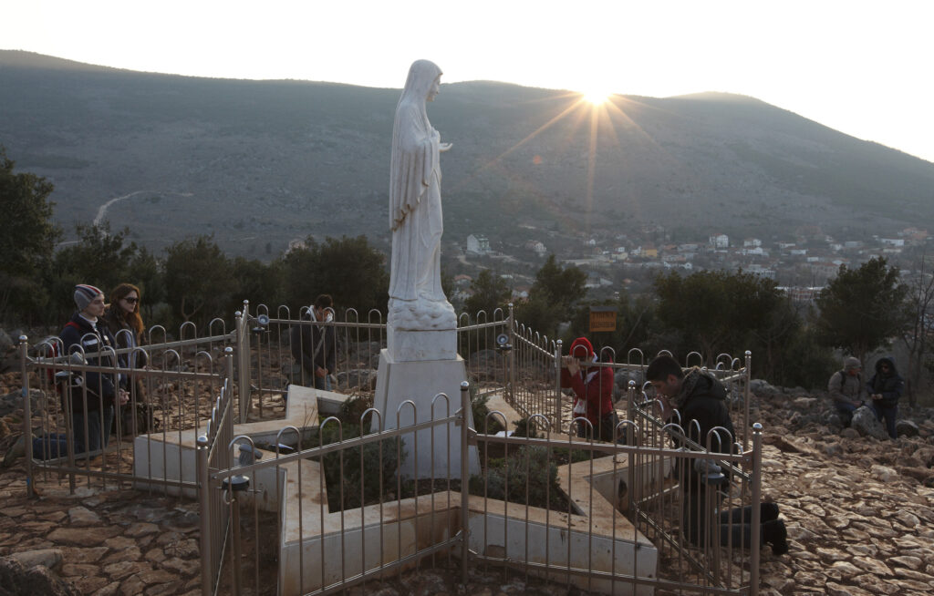 Pilgrims pray around a statue of Mary on Apparition Hill in Medjugorje, Bosnia-Herzegovina, Feb. 26. The site is where six village children first claimed to see Mary in June 1981. A Vatican-appointed commission is studying the alleged Marian apparitions at Medjugorje. CNS photo/Paul Haring)