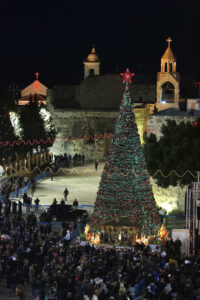 People surround a Nativity scene set under a large Christmas tree in Manger Square in the West Bank town of Bethlehem Christmas Eve 2012. The Church of the Nativity, seen in back, is revered as the site of the birth of Jesus. (CNS photo/Ammar Awad, Reuters)