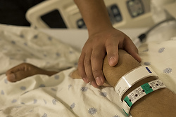 Seminarian Leo Trujillo touches the hand of seminarian William Carmona in an intensive care room at Christus Santa Rosa Medical Center in San Antonio Sept. 7. Bishop David R. Choby of Nashville, Tenn., and others from the diocese traveled to San Antonio to ordain Carmona as a priest as the young man lay dying of cancer. (CNS photo/Rick Musacchio, Tennessee Register)