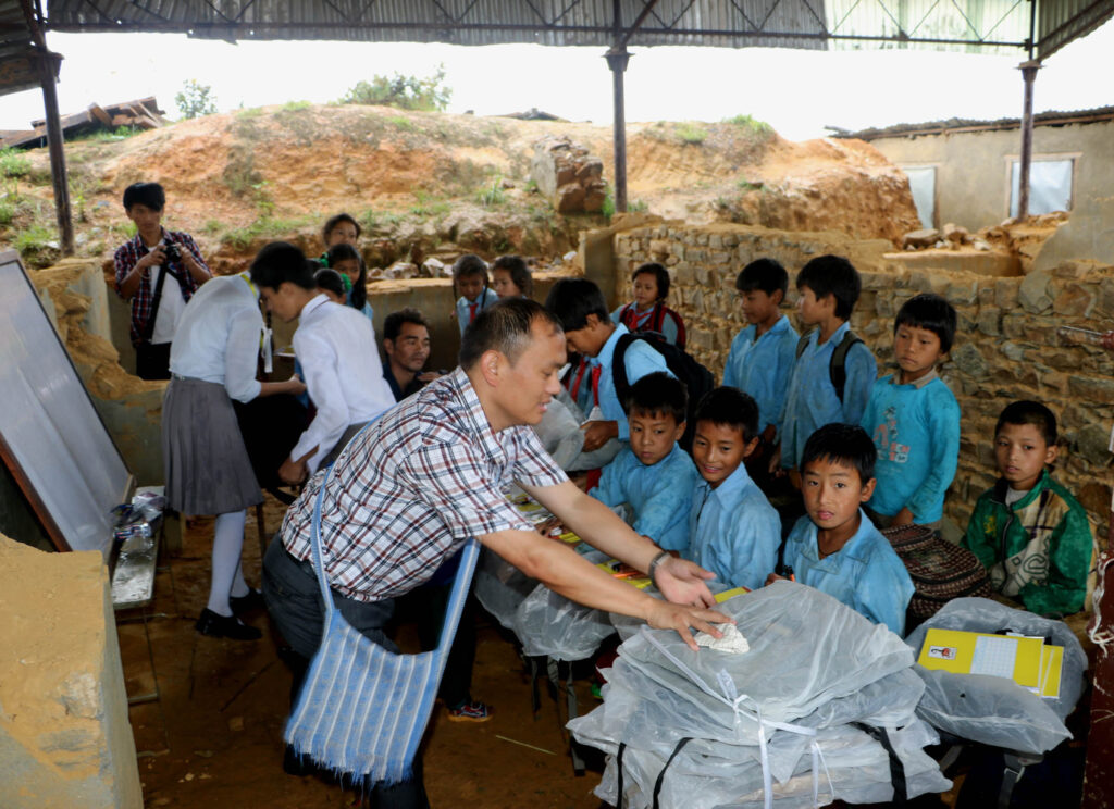 Salesian Father Savio Rai helps distribute school materials to students in a government-run school in Chaghare, Nepal, July 9. The school was damaged in the April 25 earthquake, which destroyed more than 25,000 classrooms in nearly 8,000 schools. (CNS photo/Anto Akkara)
