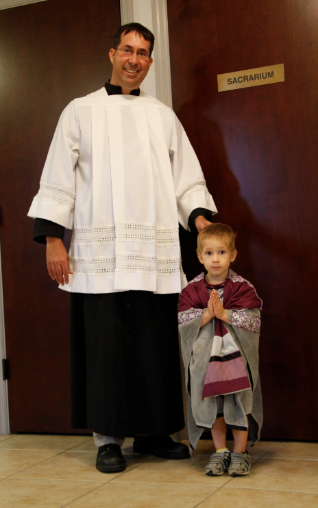 Adam Richards and his son, Andrew — showing off his pretend priest vestments — pose in the sacristy at St. Thomas the Apostle Aug. 29. The Richards say their home life and the good example of Catholic friends has fostered their son’s love for the Church. (Ambria Hammel/CATHOLIC SUN)