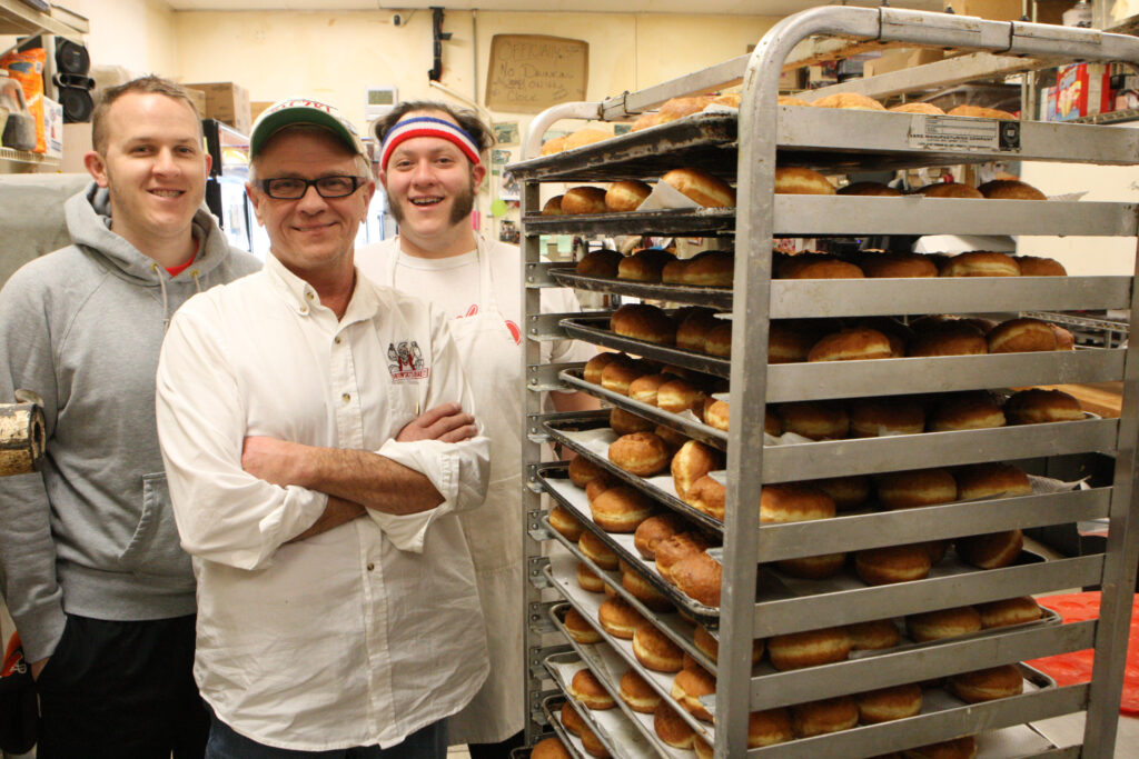 Tim Kiedrowski, center, owner of Kiedrowski's Simply Delicious Bakery, with sons, Tim, left, and Michael, are shown Jan. 18 with a rack of Polish-style doughnuts, known as "paczki." The doughnuts are a tradition in the days before Lent. (CNS photo/Dennis Sadowski)